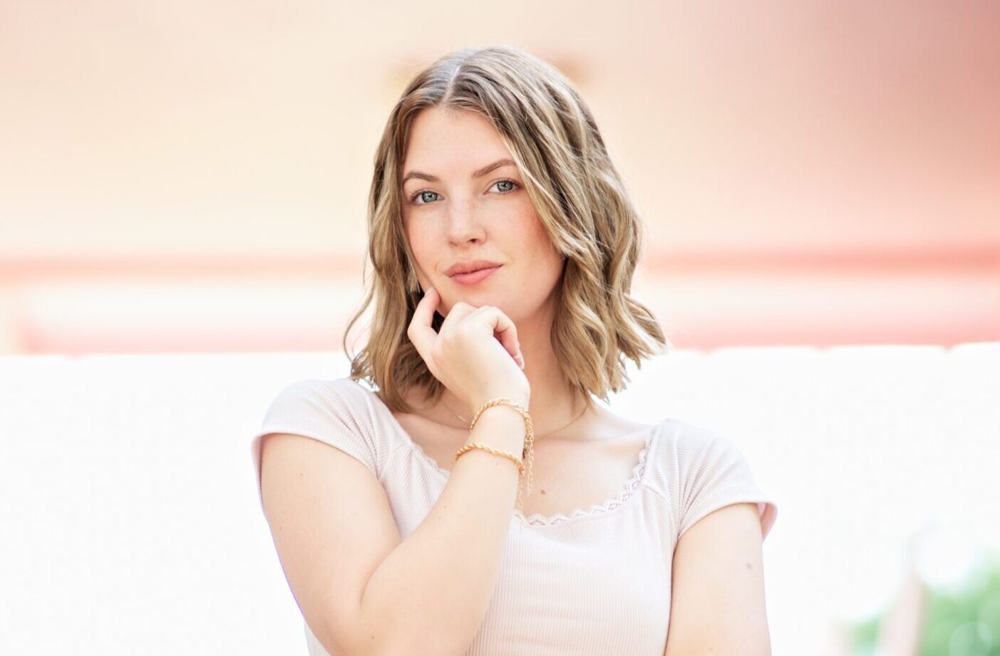 High school senior girl with wavy blonde hair poses confidently on pink stairs wearing a light pink cropped top and light wash jeans.