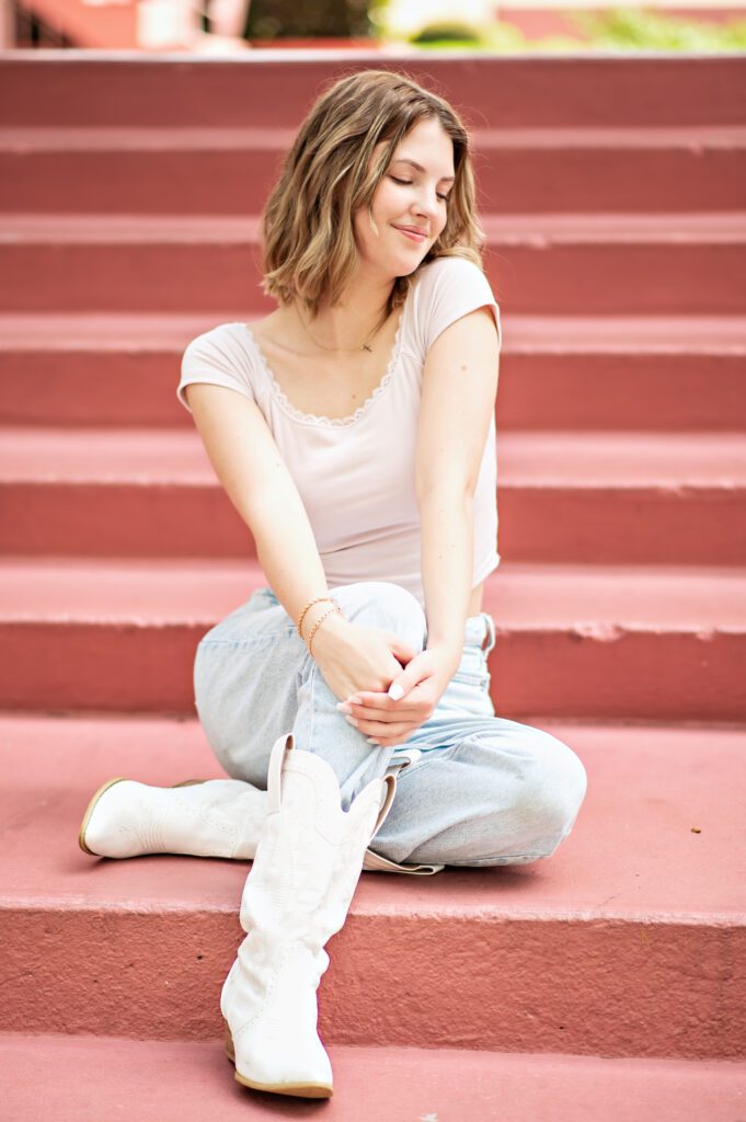 beautiful senior girl with short blond hair sitting on steps of pink iconic building in winter park