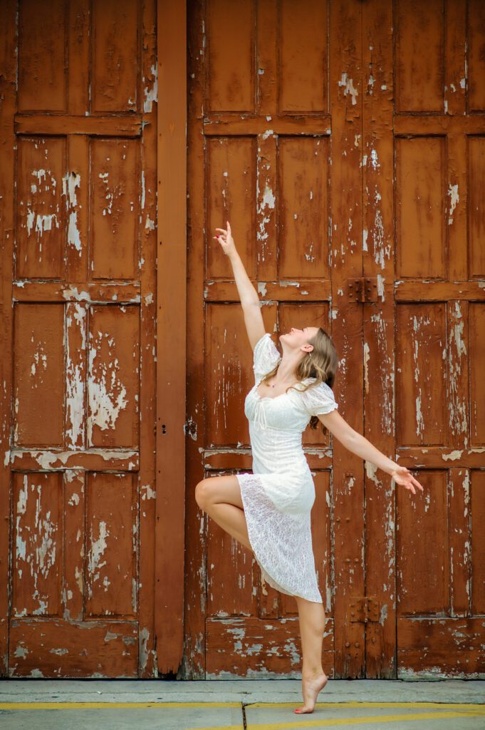 Senior girl posing in a dance pose for senior pictures in a white dress in an urban location in Winter Garden. 