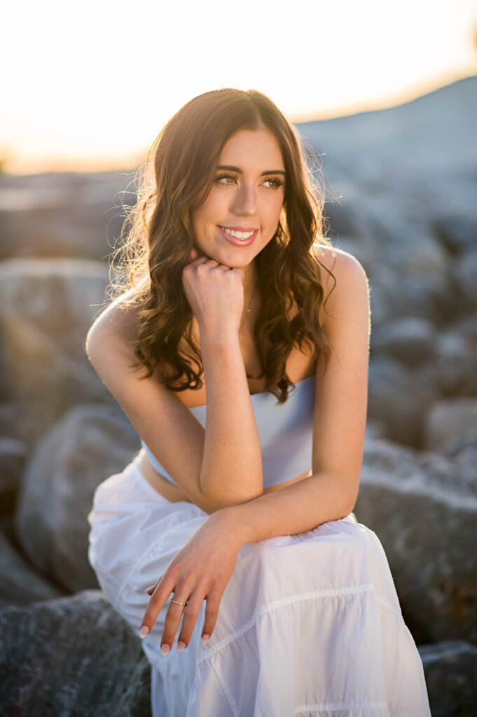 Orlando Senior Pictures at a beach sitting on rocks with a white skirt and blue top