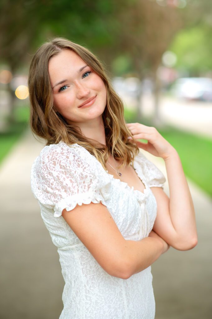 Senior pictures of young lady with brown wavy hair in a white dress in downtown Winter Garden Florida. 