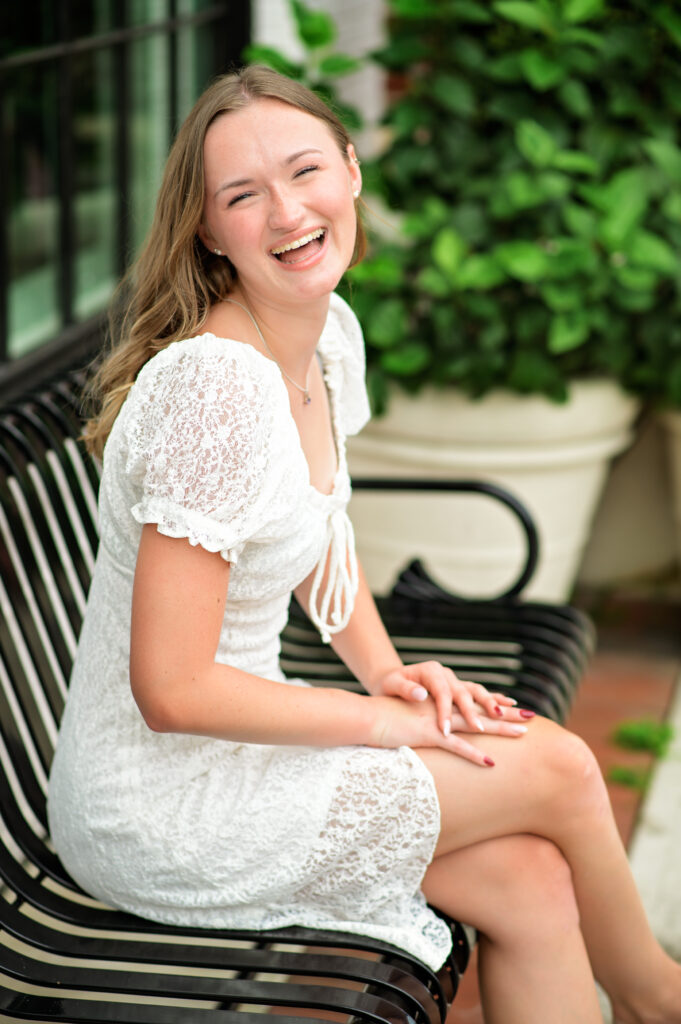 Senior pictures of young lady with brown wavy hair in a white dress in downtown Winter Garden Florida. 