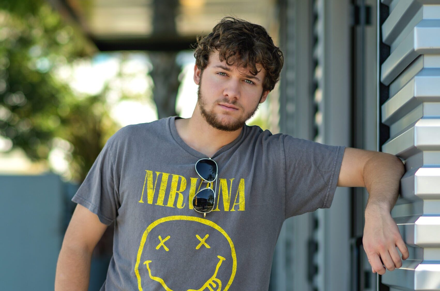 Senior boy leaning against a modern building in Orlando, wearing jeans and a t-shirt with a confident stance.