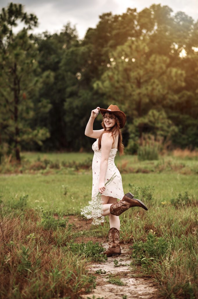 Senior girl adjusting her hat with wind blowing dress softly around her