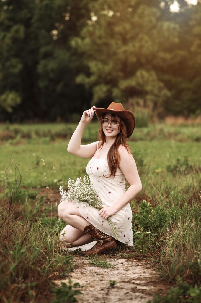 Senior girl adjusting her hat with wind blowing dress softly around her