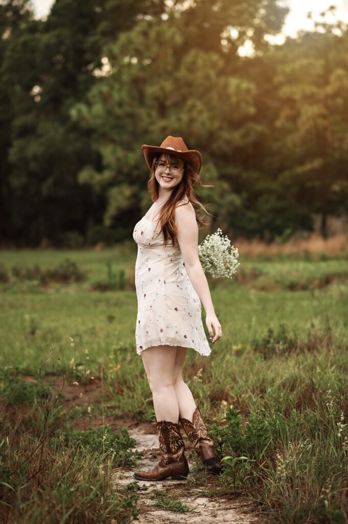 Senior girl adjusting her hat with wind blowing dress softly around her