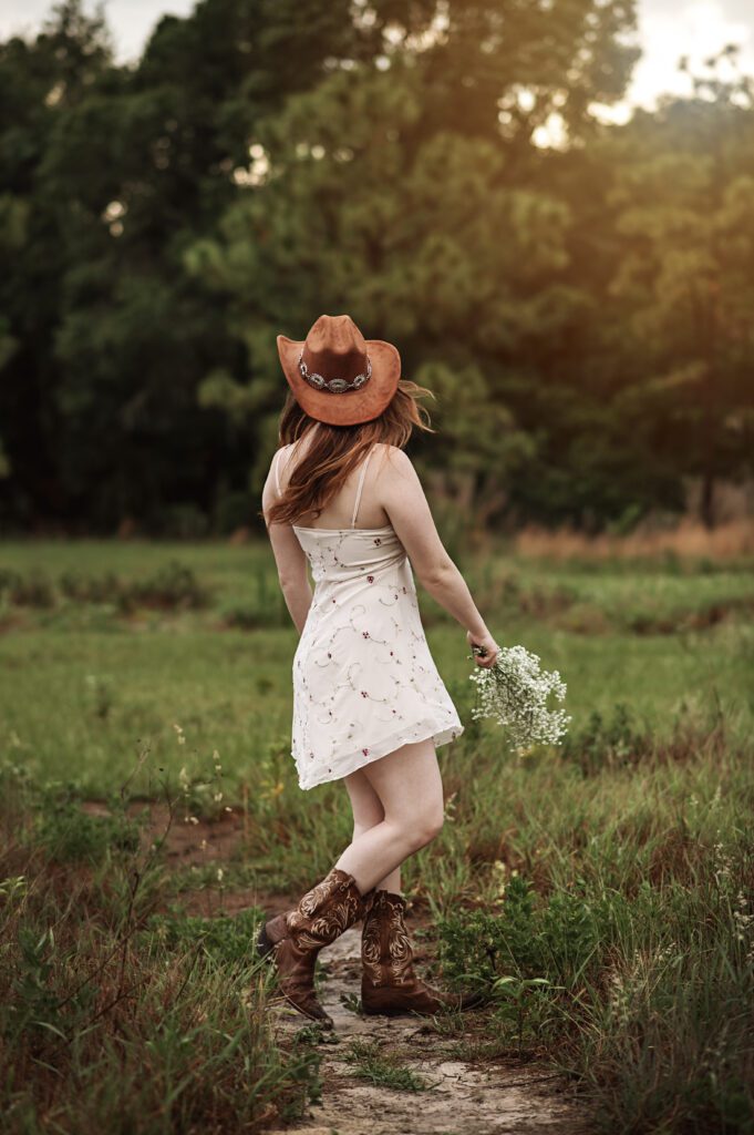 Senior girl adjusting her hat with wind blowing dress softly around her