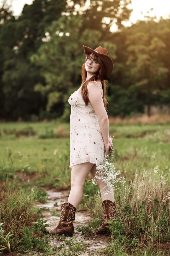 Senior girl adjusting her hat with wind blowing dress softly around her