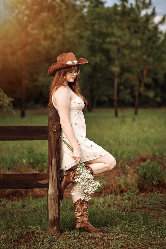 Western-inspired senior photo with girl standing near rustic wooden fence