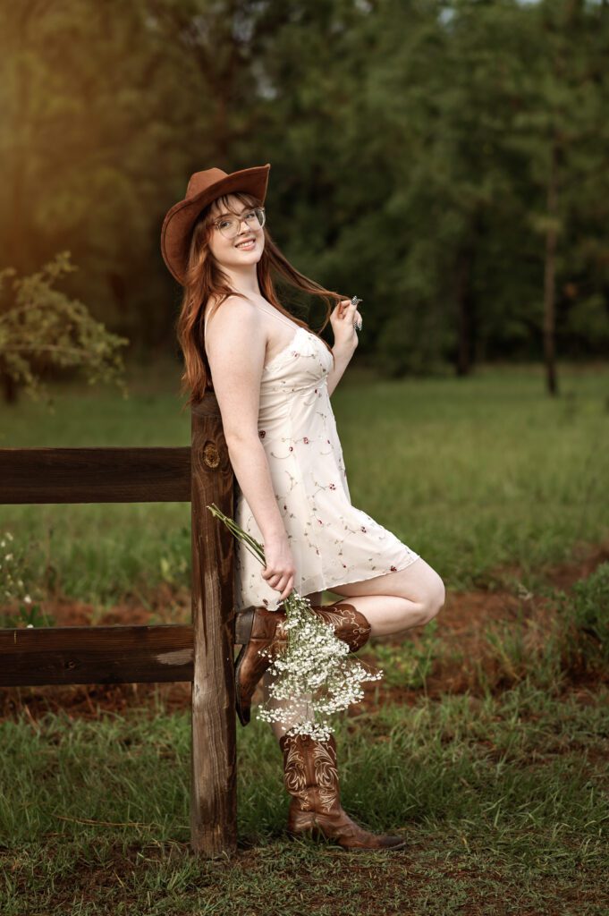 Western-inspired senior photo with girl standing near rustic wooden fence