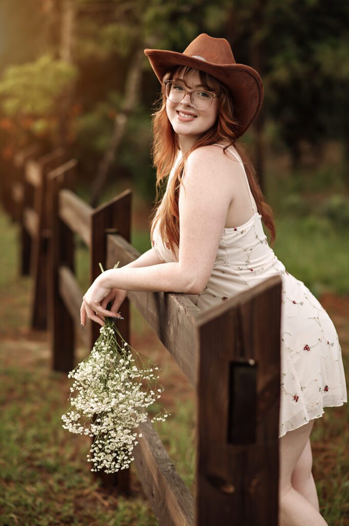 Western-inspired senior photo with girl standing near rustic wooden fence