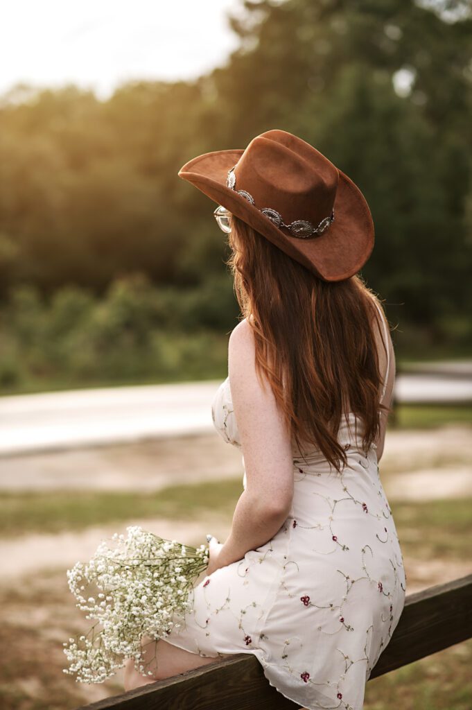 Western-inspired senior photo with girl standing near rustic wooden fence