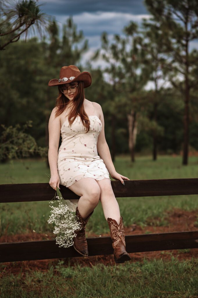 Western-inspired senior photo with girl standing near rustic wooden fence