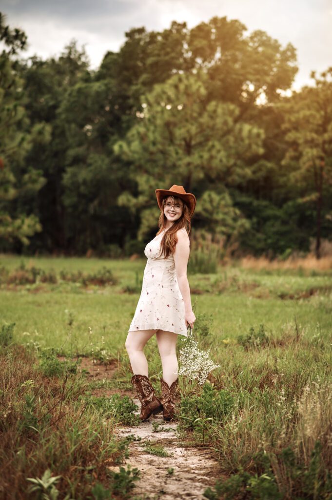Senior girl adjusting her hat with wind blowing dress softly around her