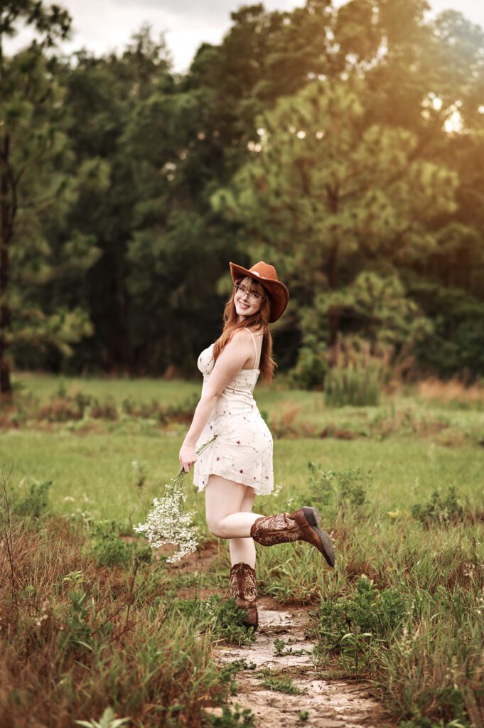 Senior girl adjusting her hat with wind blowing dress softly around her
