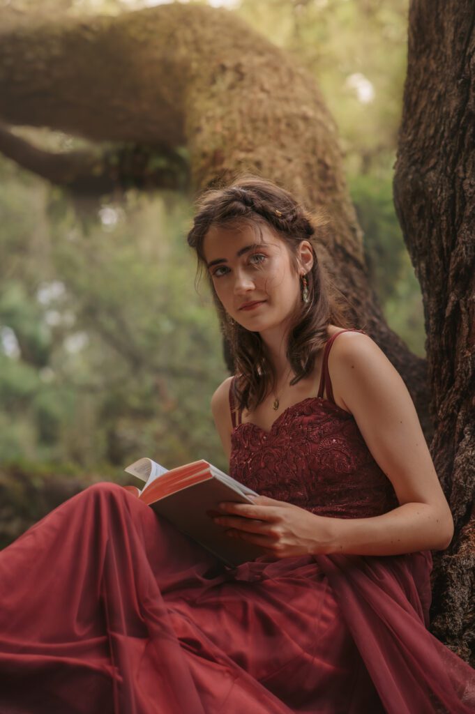 Whimsical portrait of a senior reading a hardcover book while perched on a tree branch