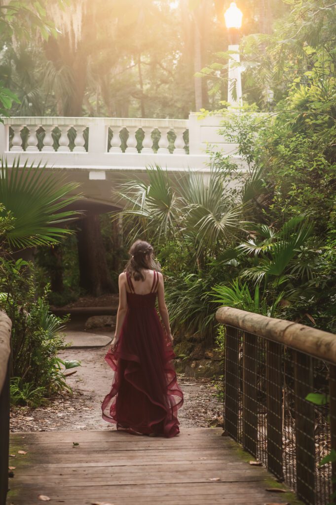 Dreamy photo of a senior waling across a wooden bridge in a sun-dappled garden in Orlando FL