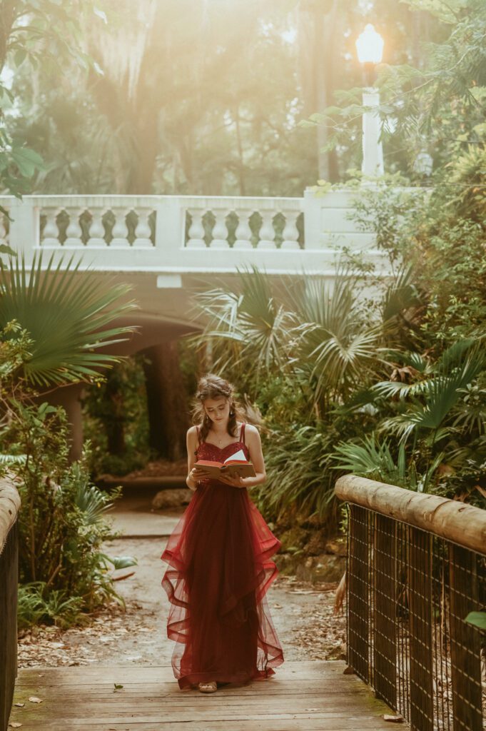 Dreamy photo of a senior looking down at her book while standing in a sun-dappled garden in Winter Park FL