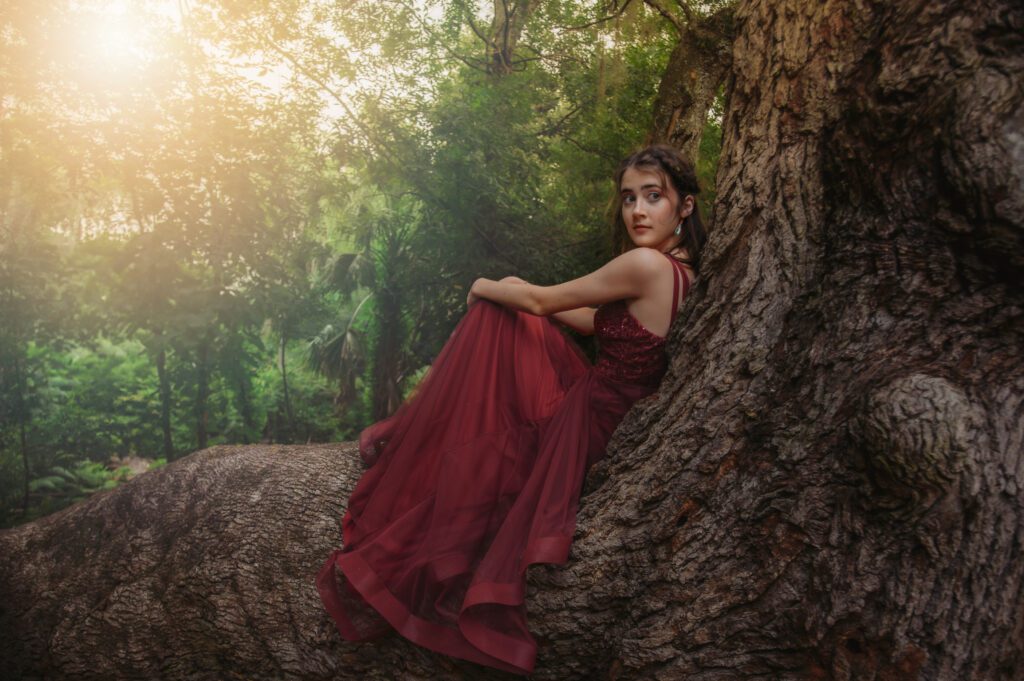 Senior sitting at the base of a large treewith a relaxed expression during a whimsical golden hour shoot