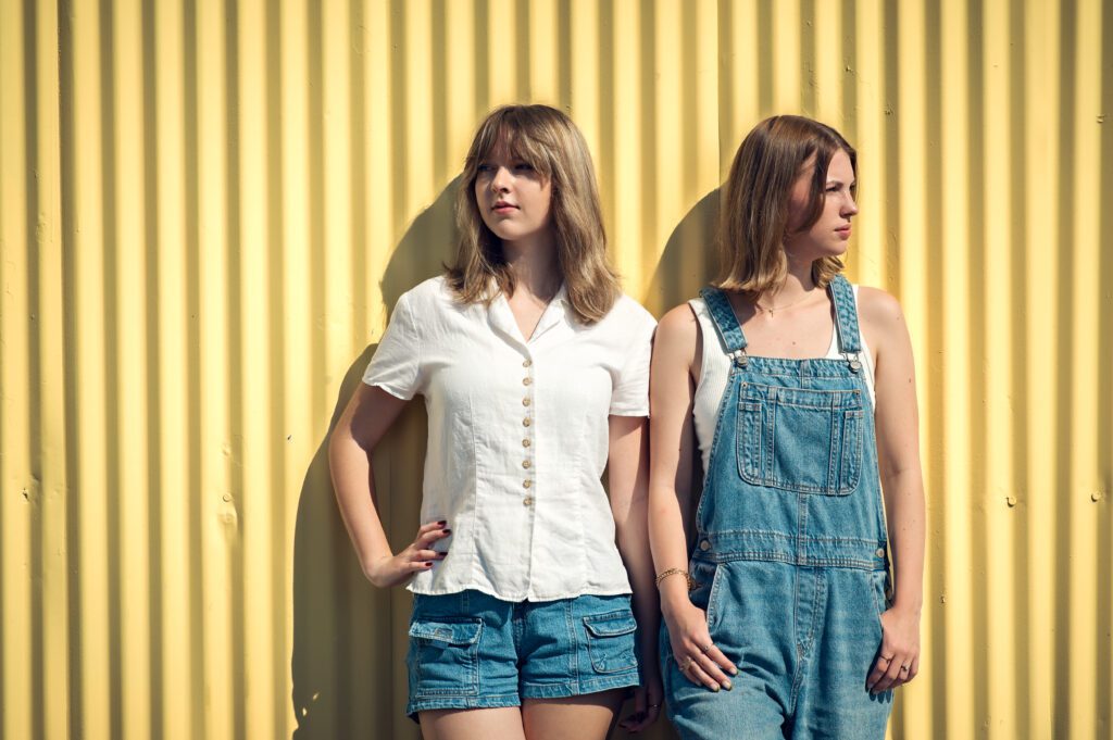 Horizontal image of senior girls leaning against a yellow background wall, styled in casual denim in Winter Garden