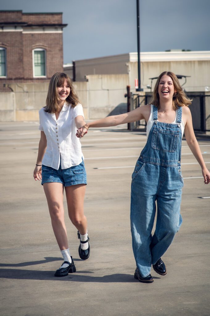 Two best friends laughing and walking across a rooftop in Downtown Winter Garden during a senior photo session