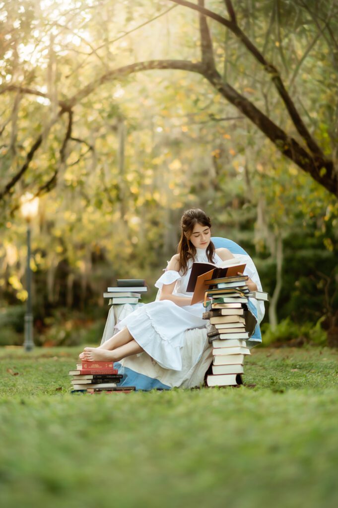 Senior girl in a chair surrounded by books while she is reading in a beautiful park in Winter Park, FL during her senior photo session with Orlando Senior Photographer, Melissa Vinsik