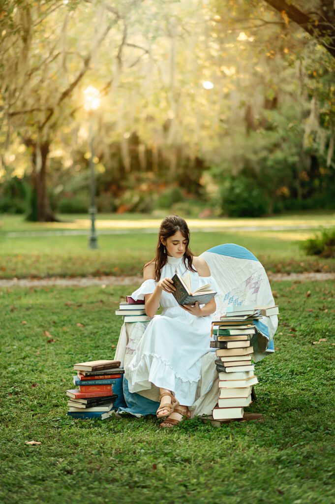 senior girl in white dress reading in a chair surrounded by books in Winter Park, Florida during her senior photo session with Melissa Vinsik Photography
