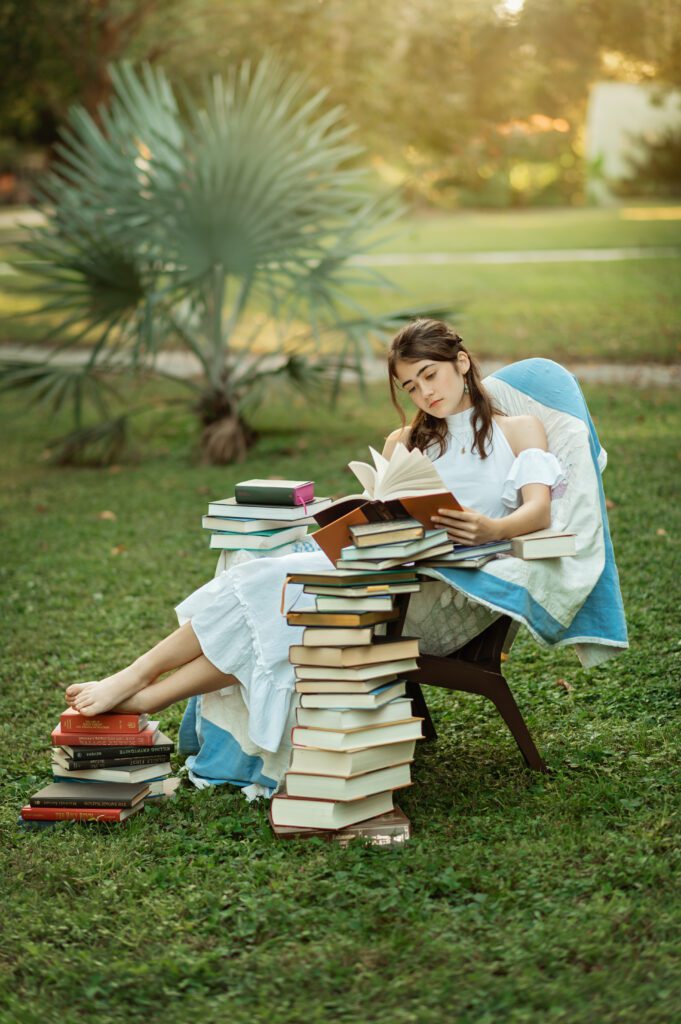 senior girl in white dress reading in a chair surrounded by books in Winter Park, Florida during her senior photo session with Melissa Vinsik Photography