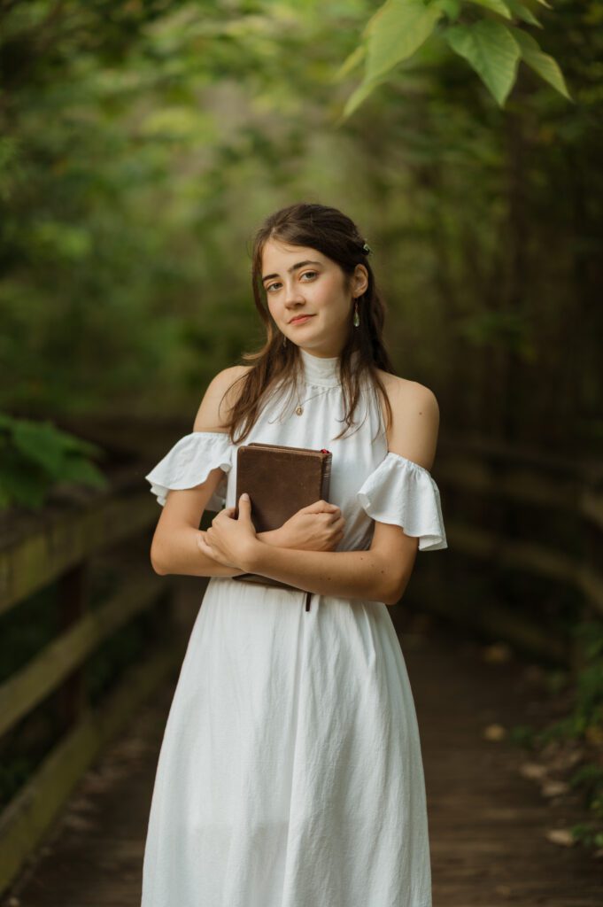 senior high school girl holding her bible on a boardwalk surrounded by greenery on a boardwalk at Mead Gardens in Winter Park, during her senior photo session with Melissa Vinsik Photography