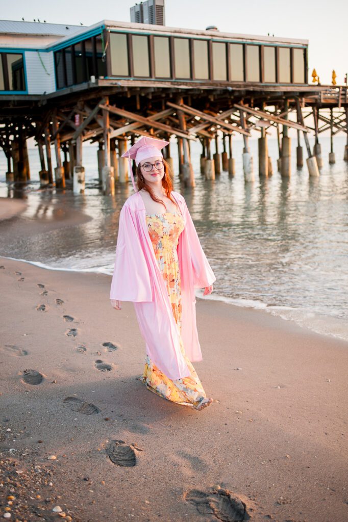 senior girl walking on the beach at Cocoa Beach in her cap and gown