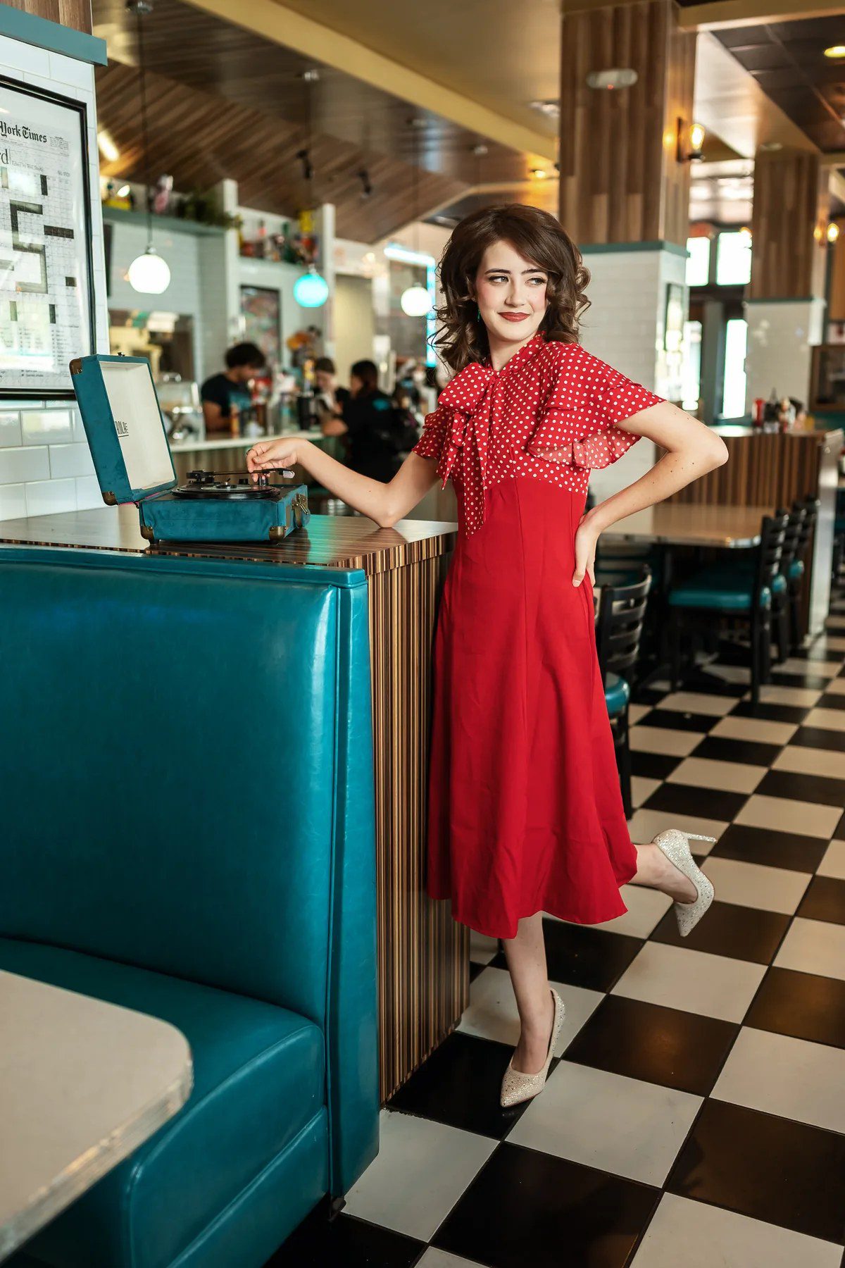 Senior portrait in a red polka-dot dress beside a teal diner booth