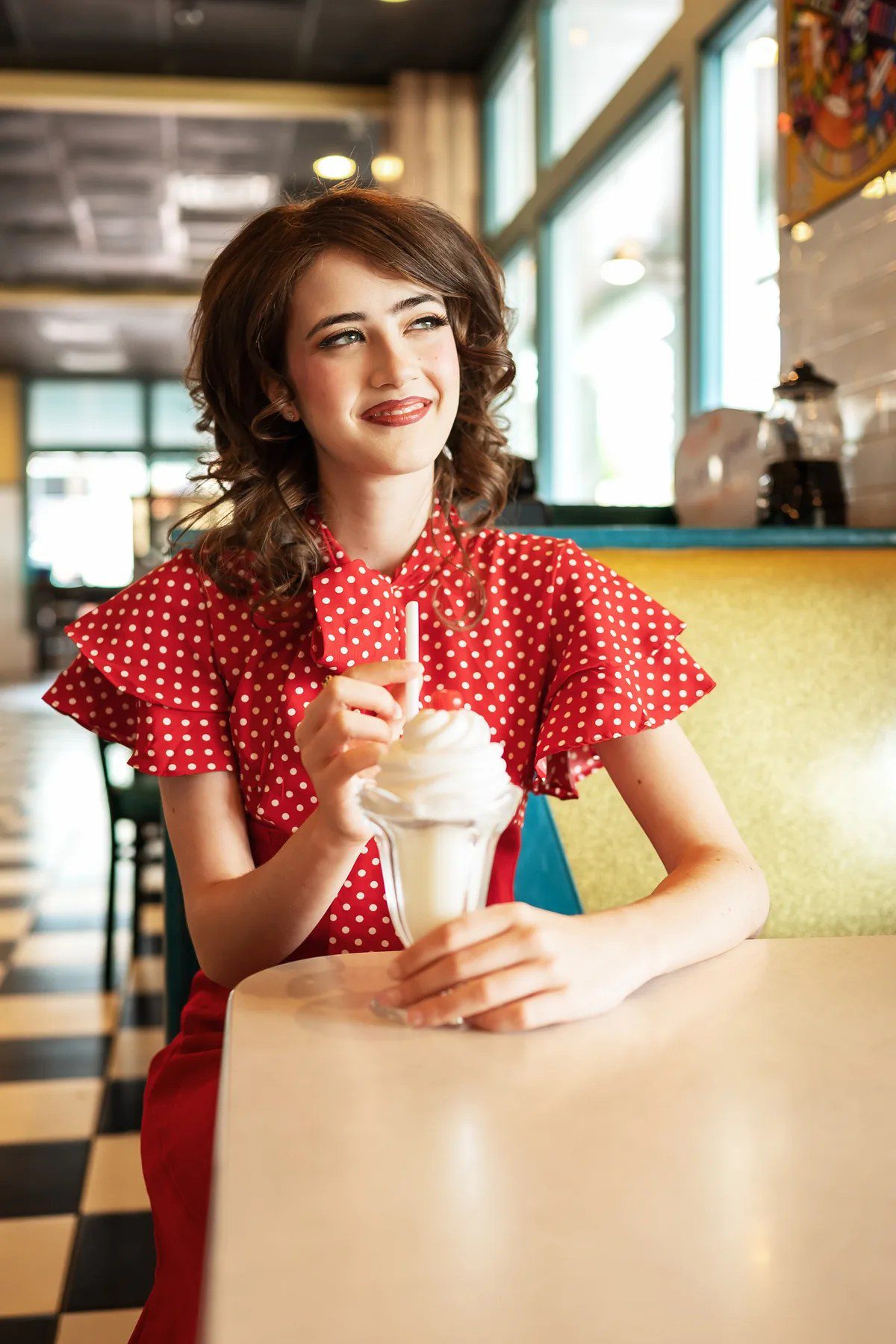 Senior in a red polka-dot dress using a vintage telephone inside a Celebration diner