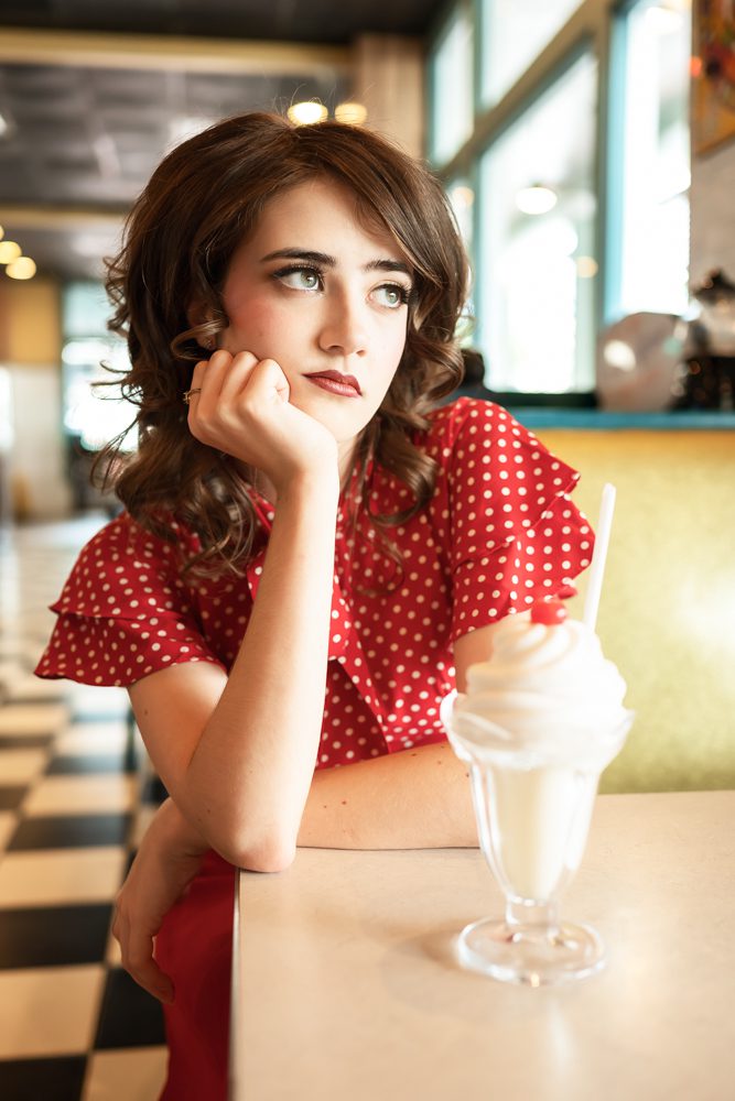 Senior in a red polka-dot dress posing with an ice cream sundae at Celebration Diner