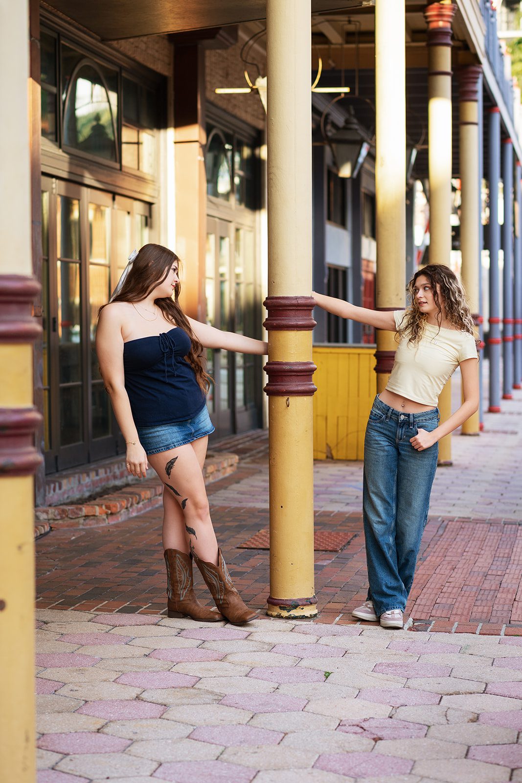 Two high school friends posing across a yellow column on Church Street in Downtown Orlando.