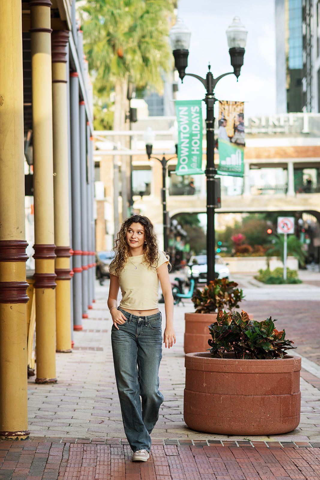 High school senior walking past a planter and Downtown Orlando banners during an urban photo session.