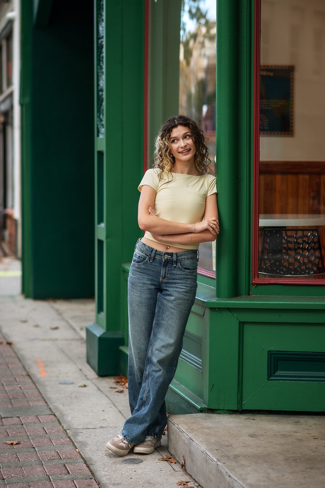 Senior girl smiling beside the green CityArts exterior in jeans and a yellow top.