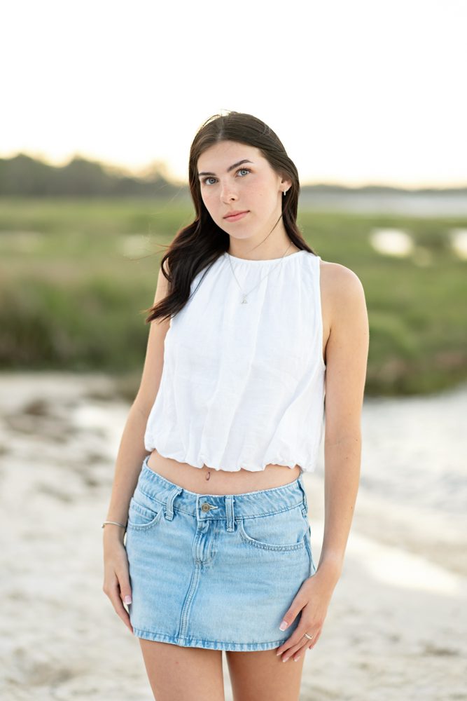 High school senior in a white top posing naturally near the water
