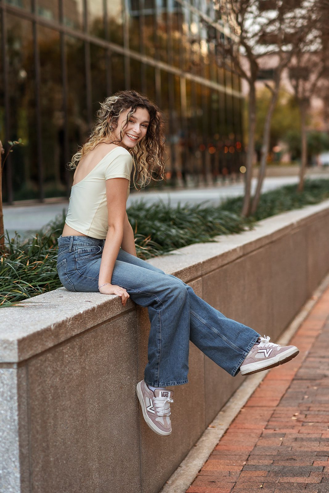 High school senior smiling while seated on a stone wall during an urban photo session.