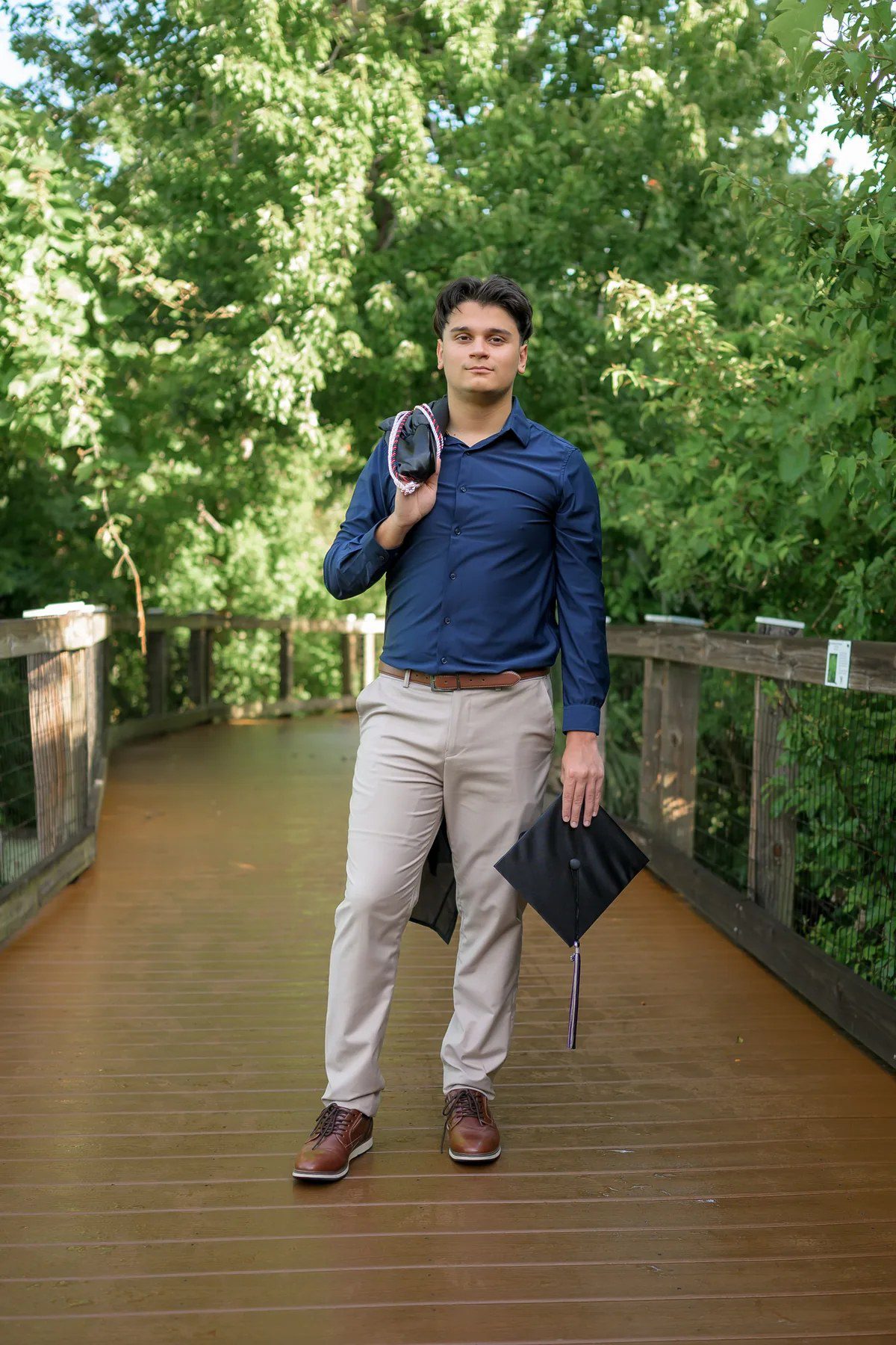 Senior graduation portrait holding a cap and gown at Oakland Nature Preserve