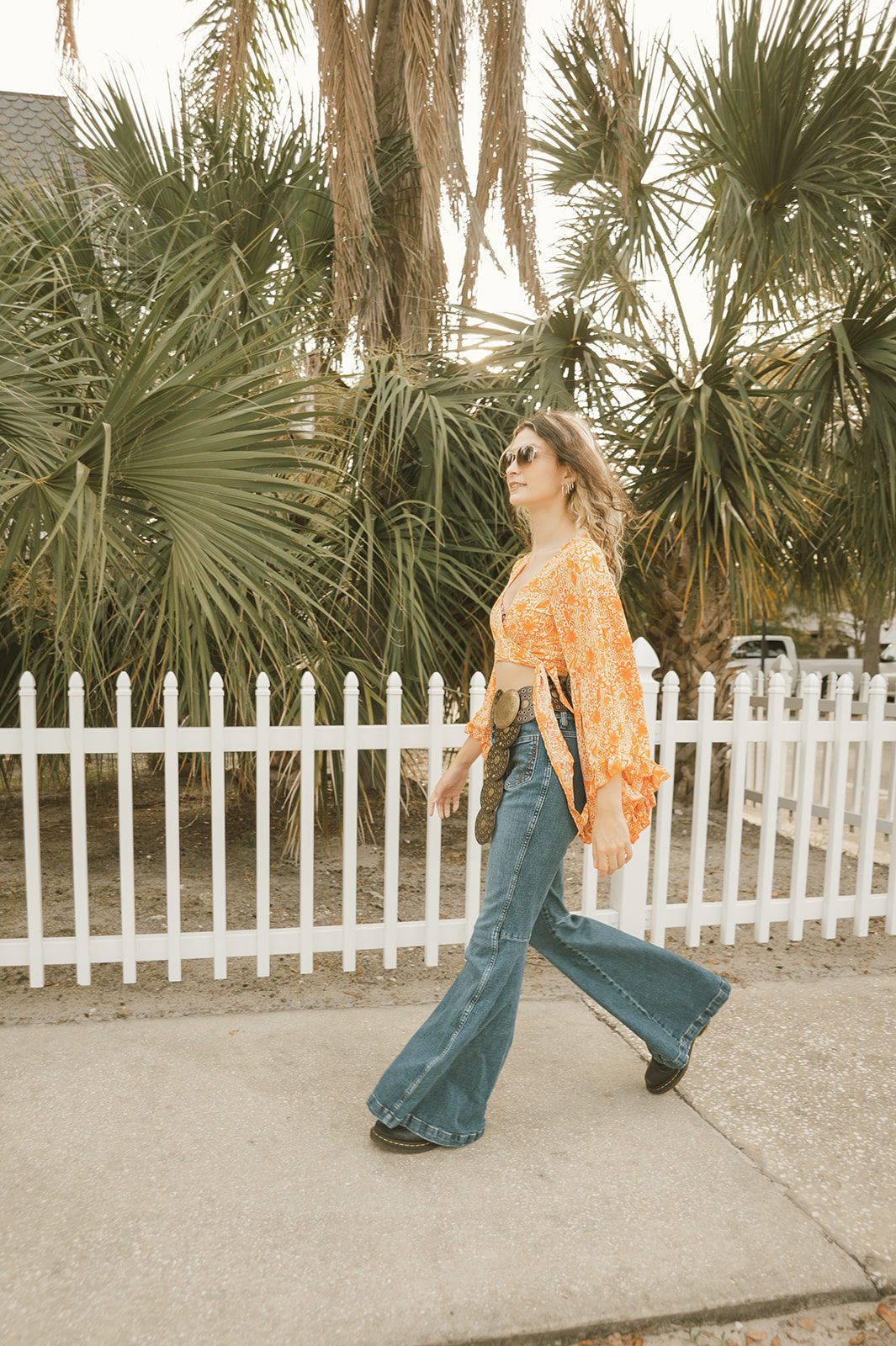 Keeleigh walking past palm trees and a white fence during a creative senior photo session in Winter Park.