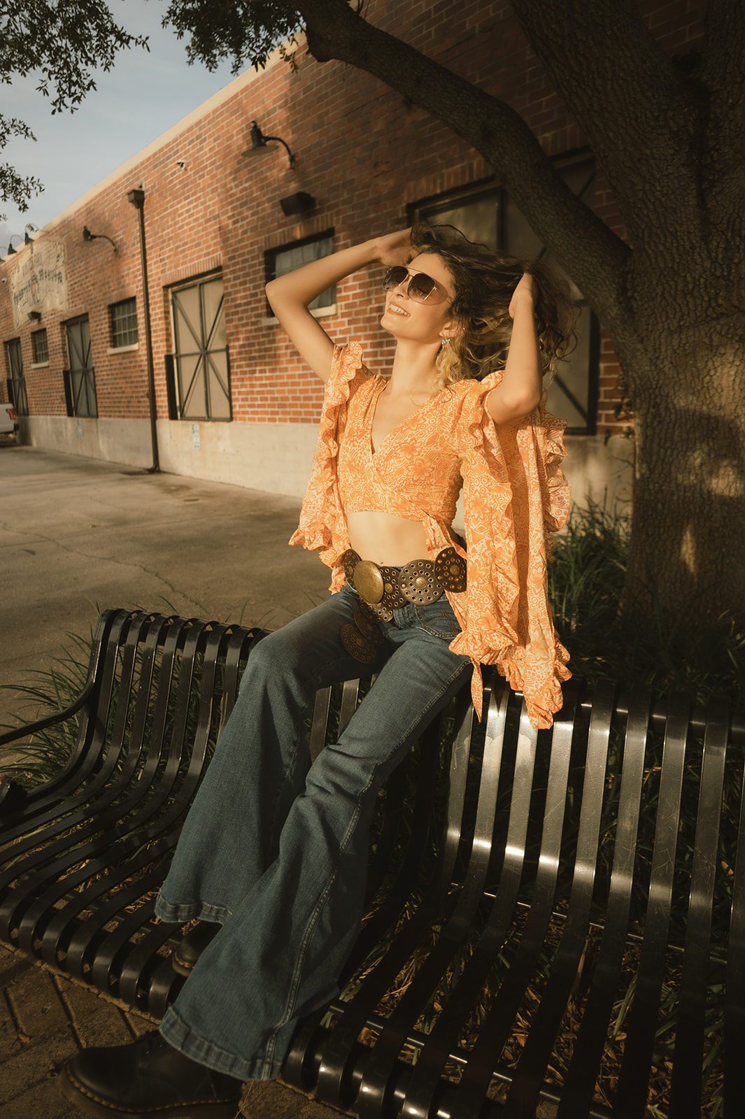 Editorial senior portrait of Keeleigh in a 1970s outfit seated by a brick building in Winter Park.