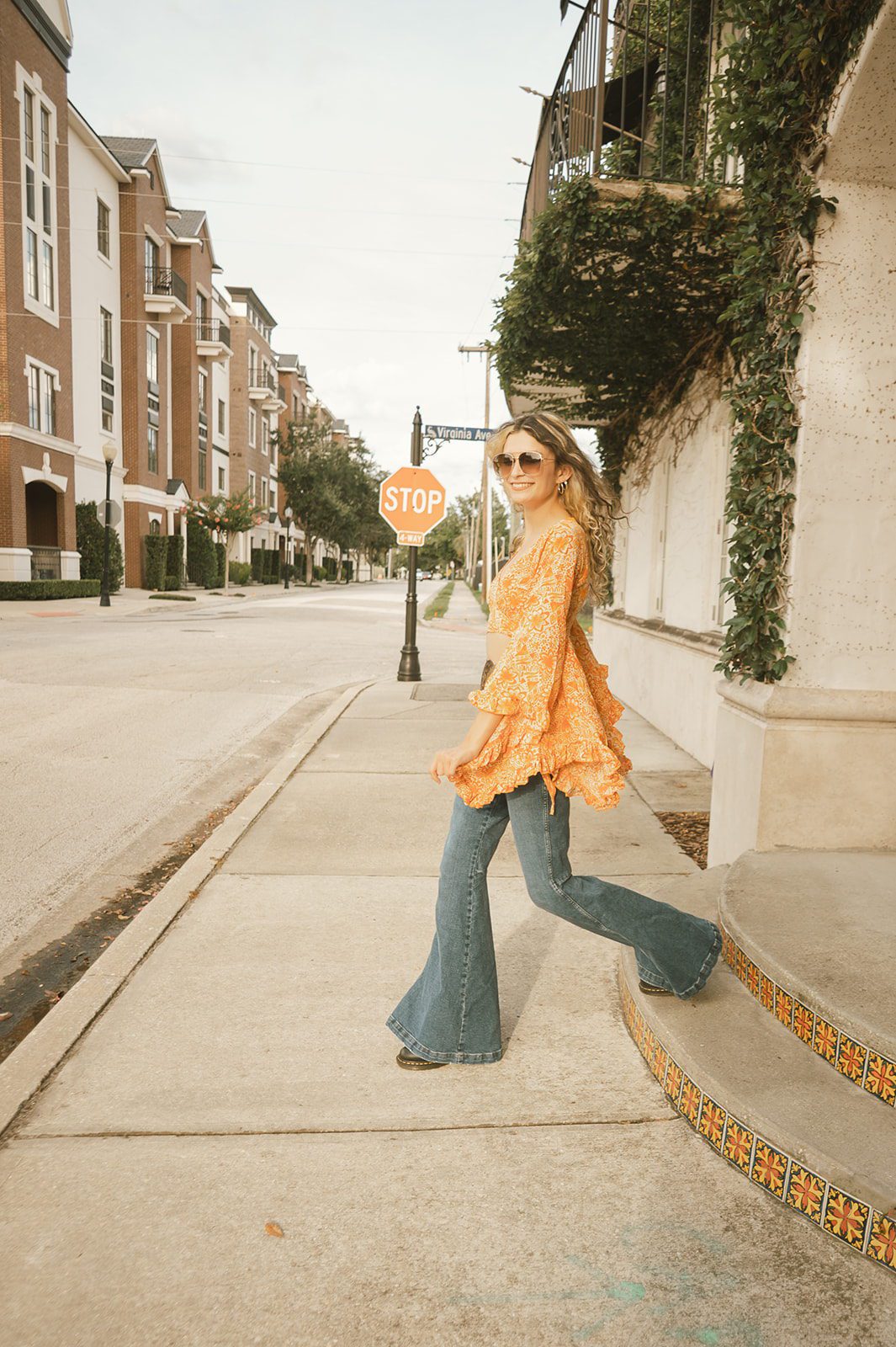 High school senior Keeleigh walking in bell bottoms and retro sunglasses during a 1970s-inspired senior session in Downtown Winter Park, Florida.