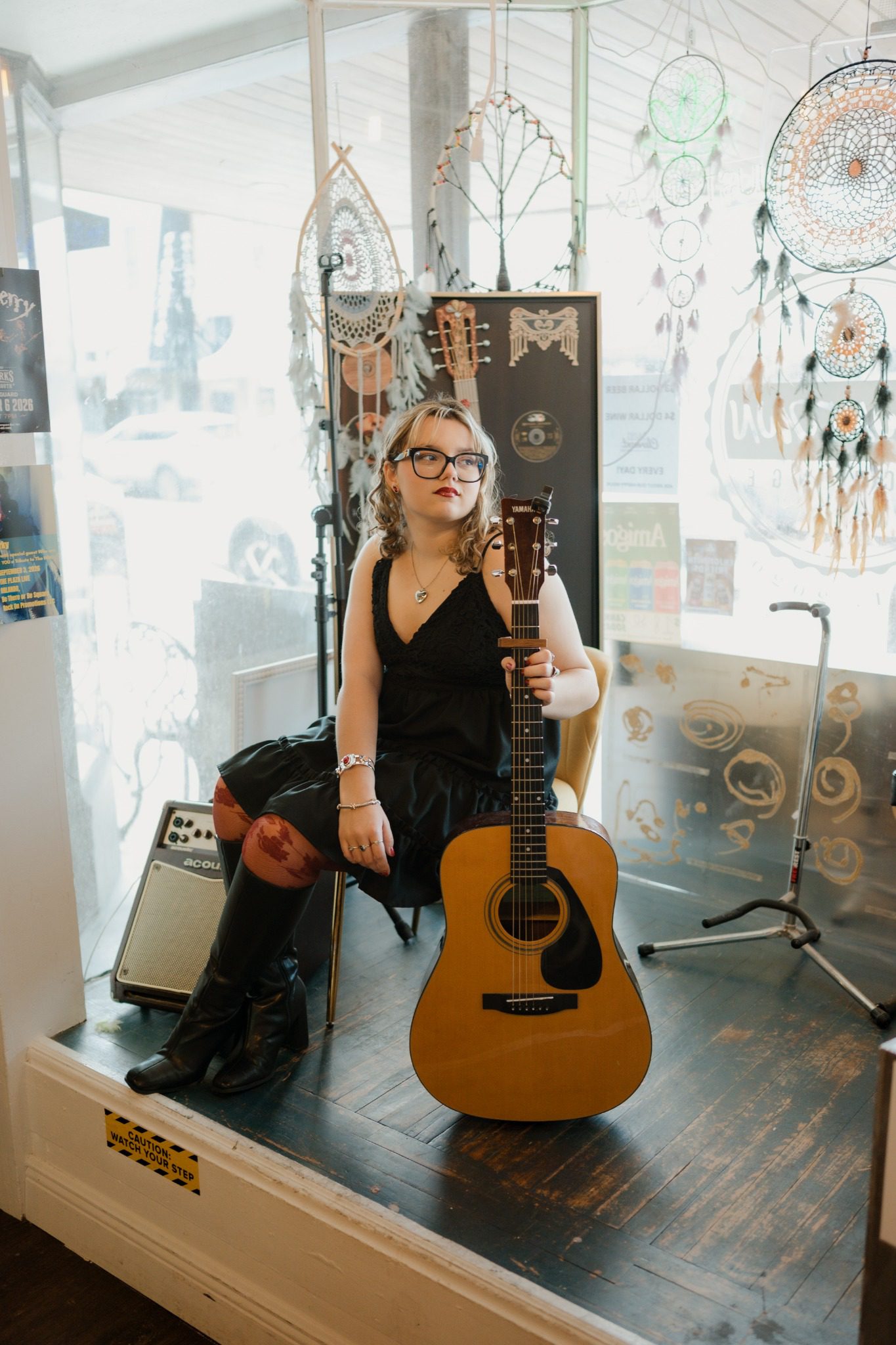 Senior walking through a Clermont record store in a black dress, red tights and tall boots