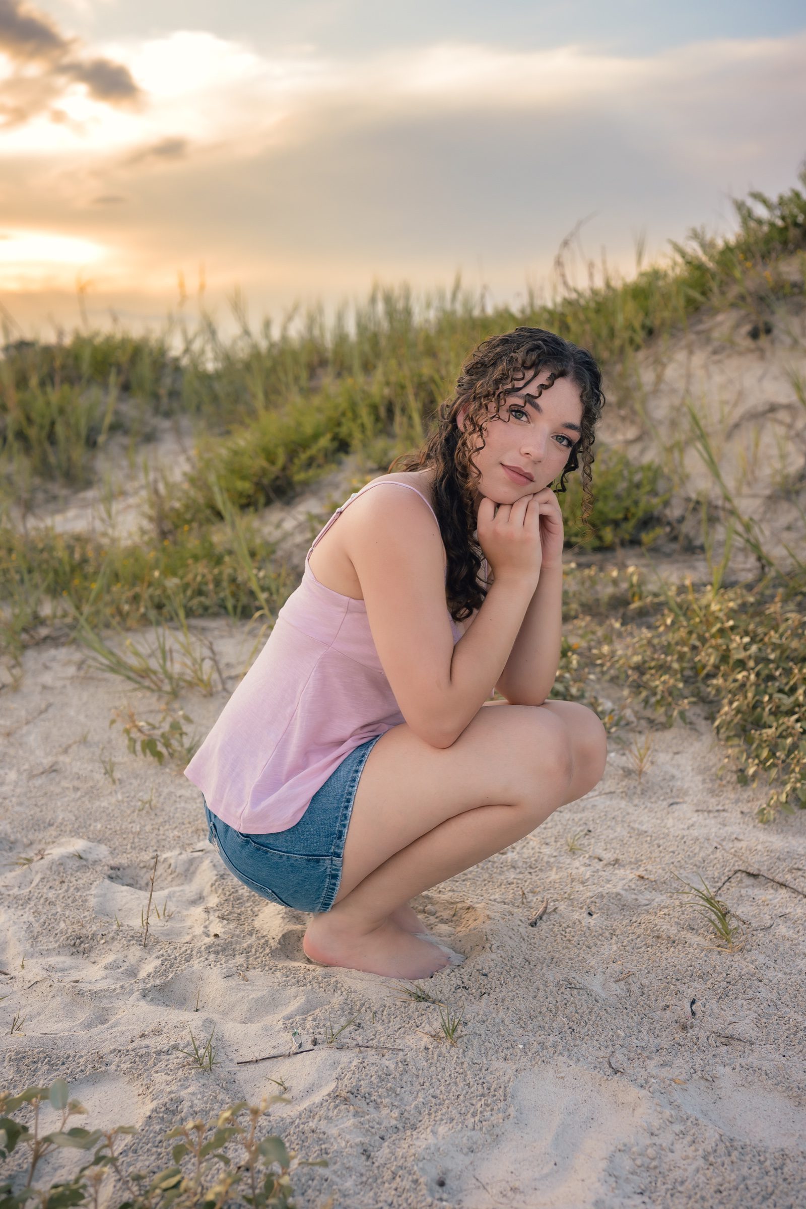 Senior in a pink top and denim skirt beside dunes on Florida’s Space Coast