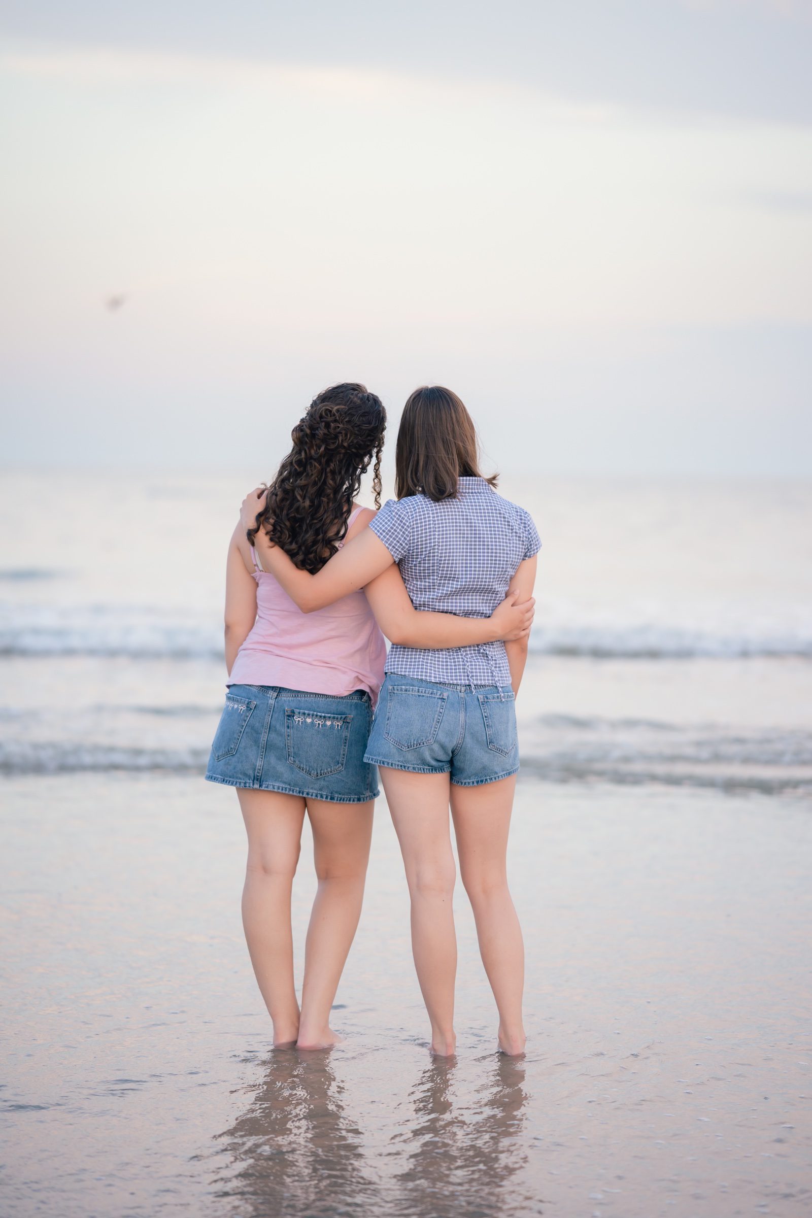 Senior and her best friend with their arms around each other, facing the ocean