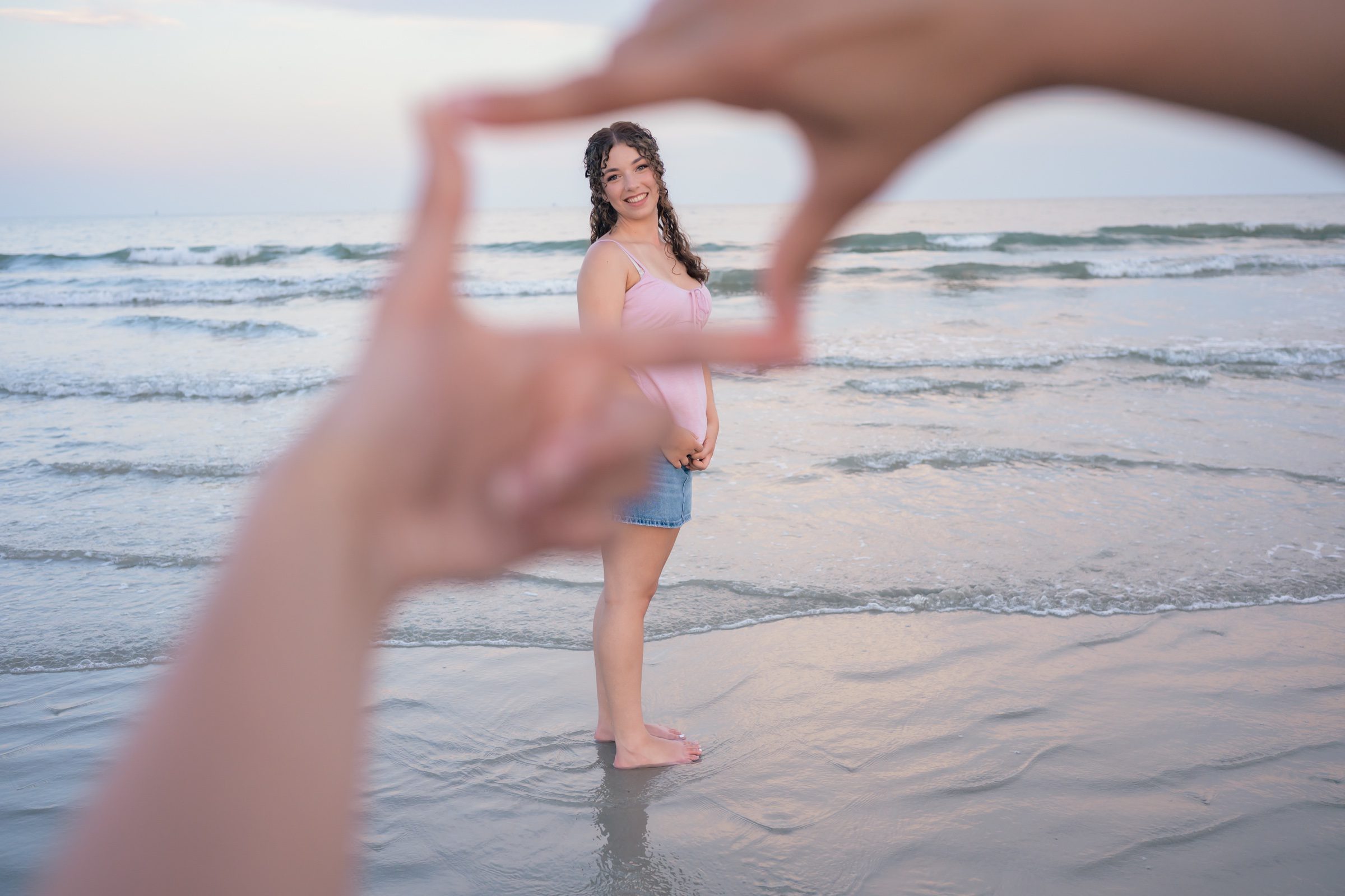 Senior on the shoreline, framed by hands in the foreground
