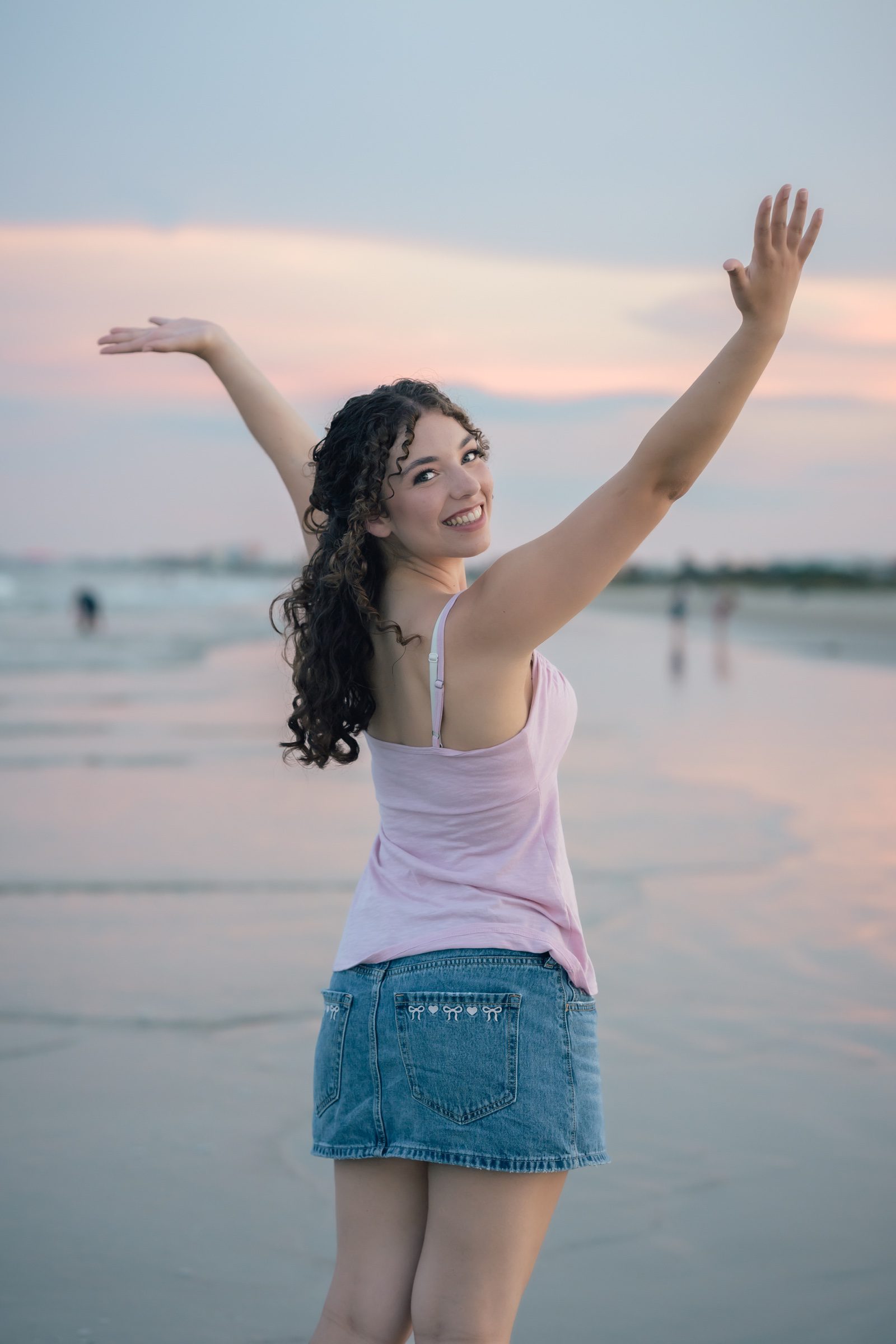 Senior raising her arms beneath a pink evening sky at Jetty Park near Cocoa Beach