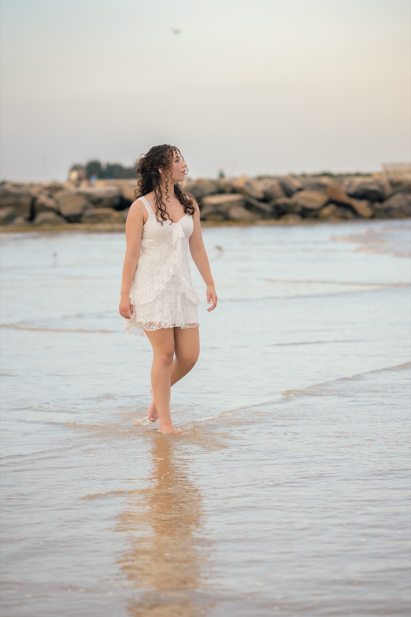 Senior walking barefoot along the shoreline with the jetty behind her