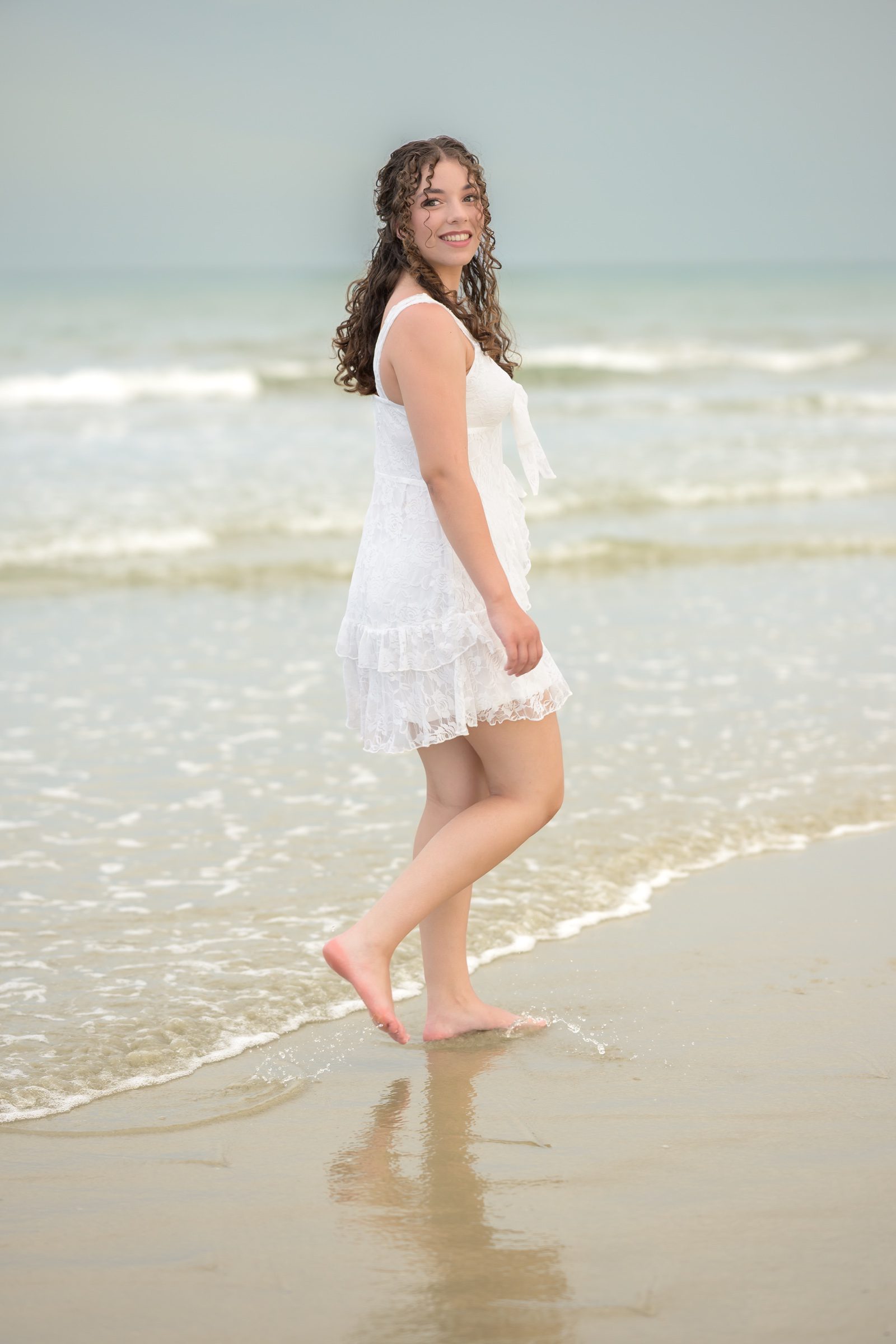 Senior in a white lace dress at Jetty Park, a beach senior picture location near Orlando