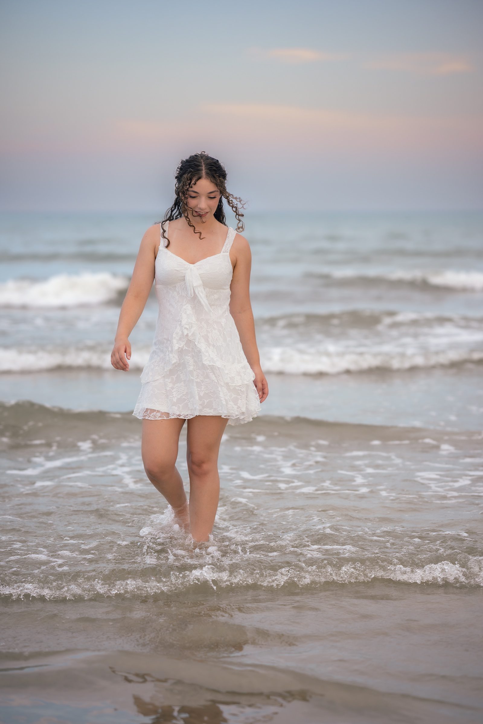 Senior looking down as she walks through the shallow surf